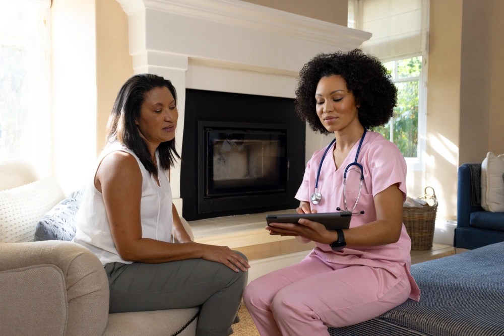 Two women enjoy time on the couch during memory care services with Thrive On Care.