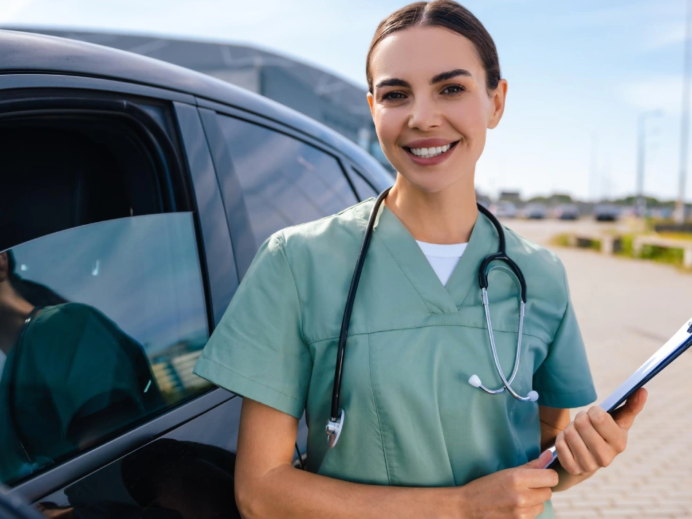 A Thrive On Care nurse stands beside a vehicle during transportation support.