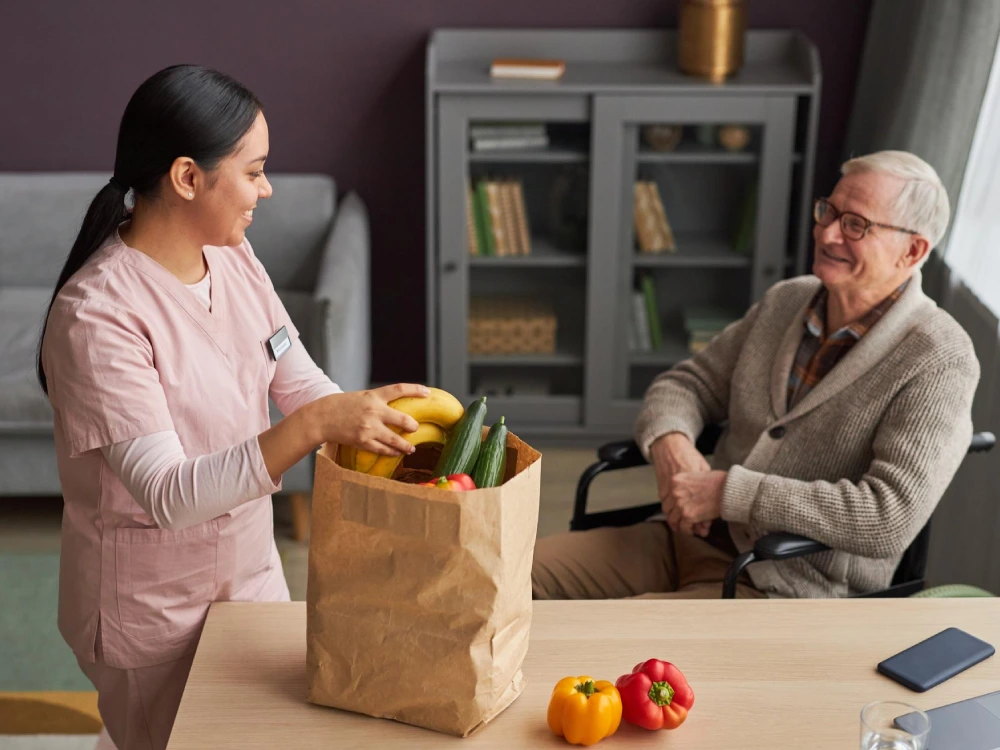 A Thrive On Care nurse helps unload groceries for an elderly patient at home.