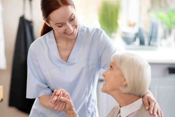 A caregiver from Thrive On Care gently holds a client’s hand while providing personal care.