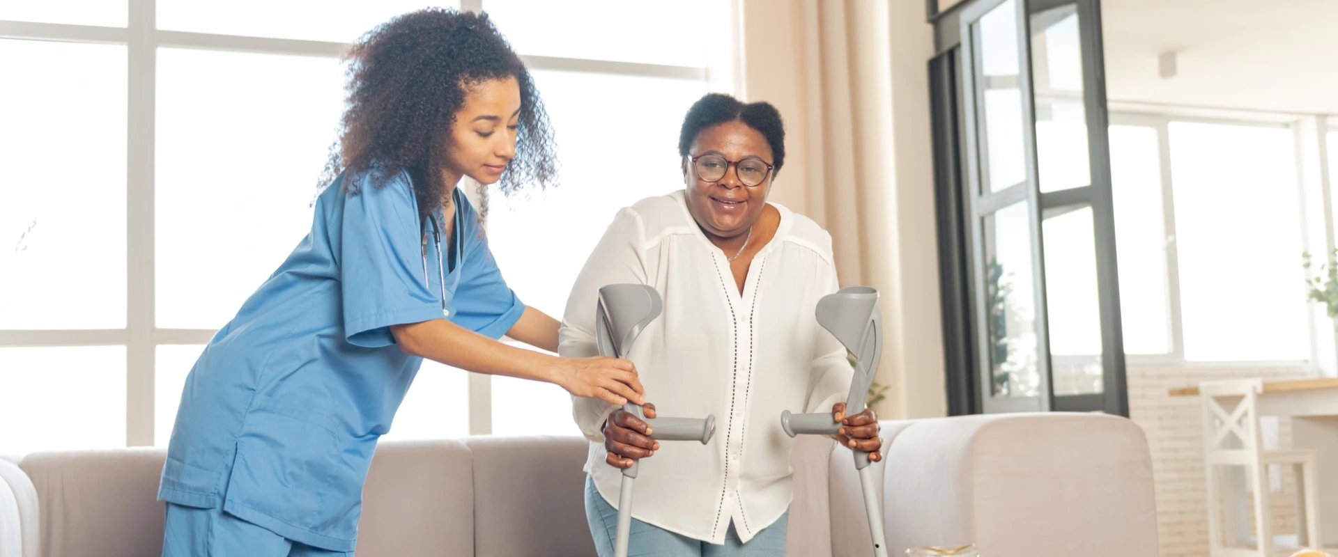 Thrive On Care caregiver assists a smiling woman with mobility support using crutches at home.